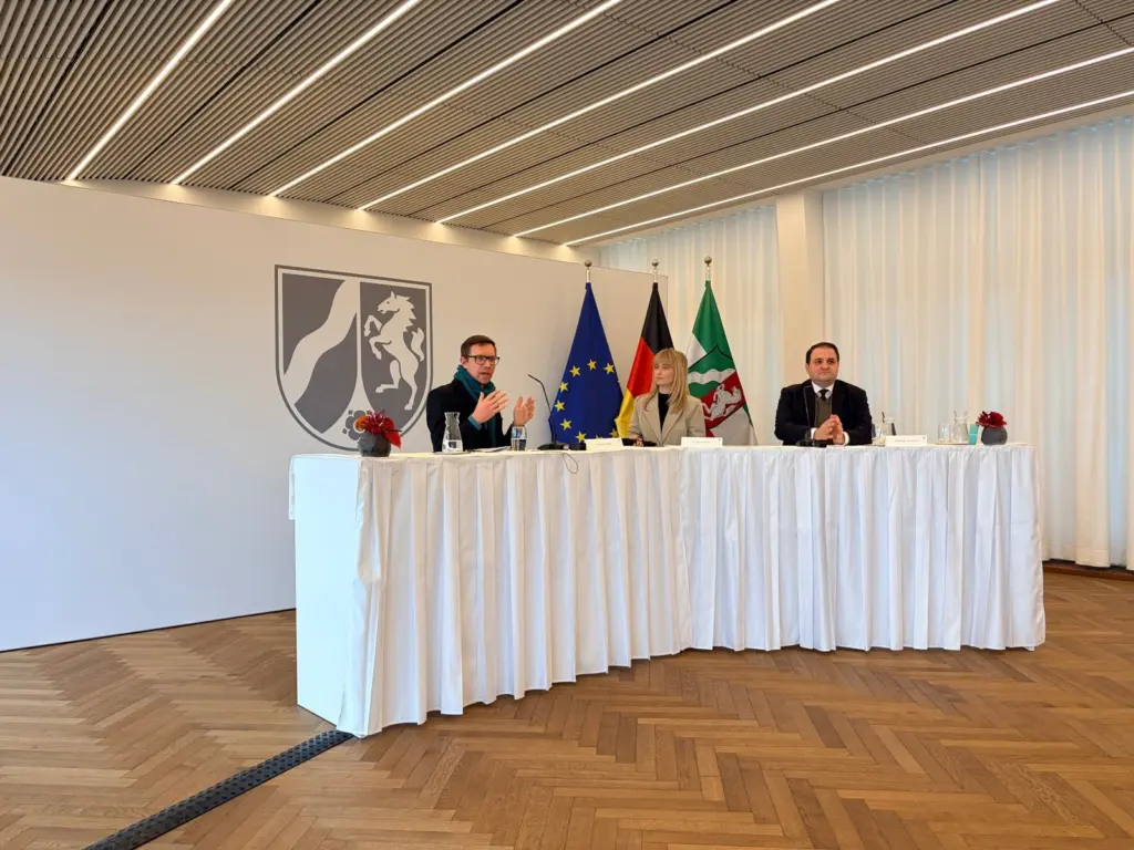 Heiner Fischer auf einem Podium vor dem Landeswappen von NRW